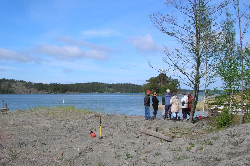 En grupp personer håller möte vid en insjöstrand och ett råmärke är redan fastsatt till hälften.